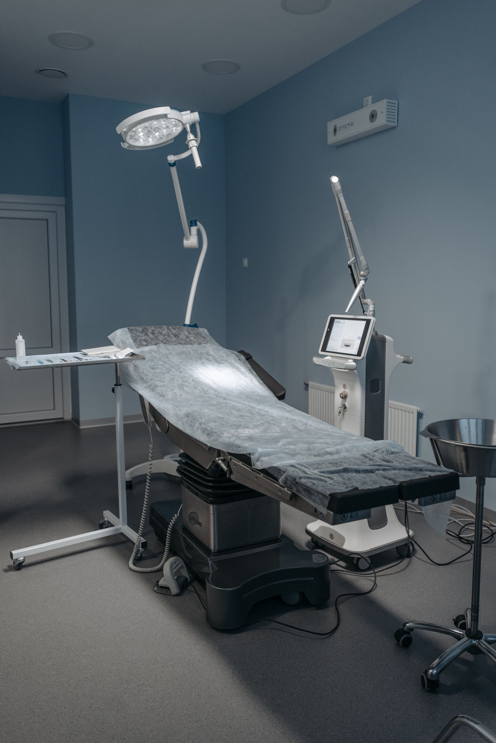Modern hospital procedure room with examination table, surgical lamp and monitoring equipment